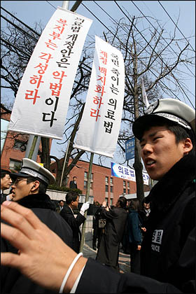 공청회에 불참한 의료단체 회원들이 정부의 의료법안에 반대하는 집회를 강행하자 만일의 사태에 대비해 경찰이 폴리스라인을 설치하는 등 행사장 입구가 다소 어우선하다.
 